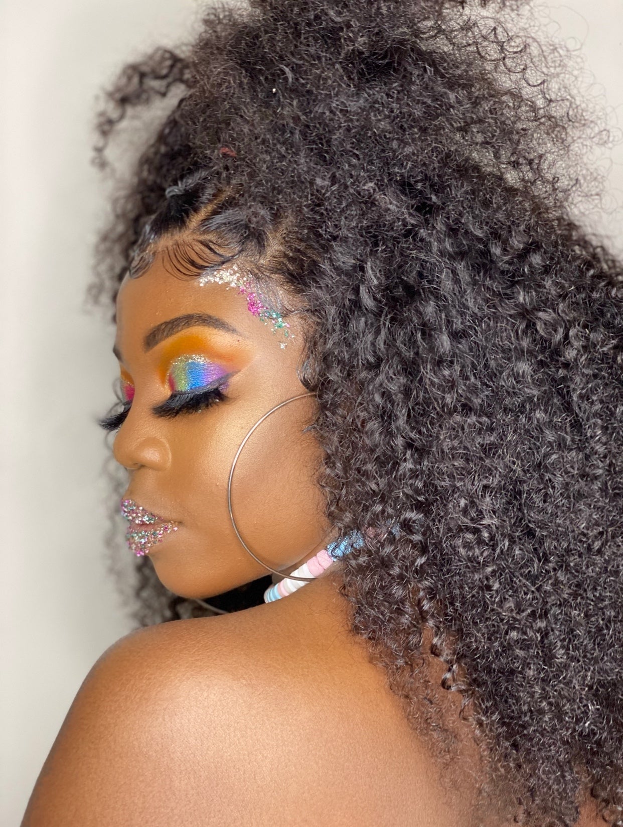 Close-up of a person with voluminous curly hair and colorful makeup.